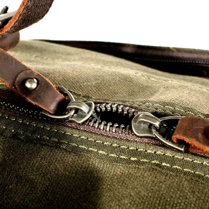 "Duffelväska för män i militärstil, vaxad canvas med läderdetaljer, rymlig med dragkedjor, stilfull och robust design."