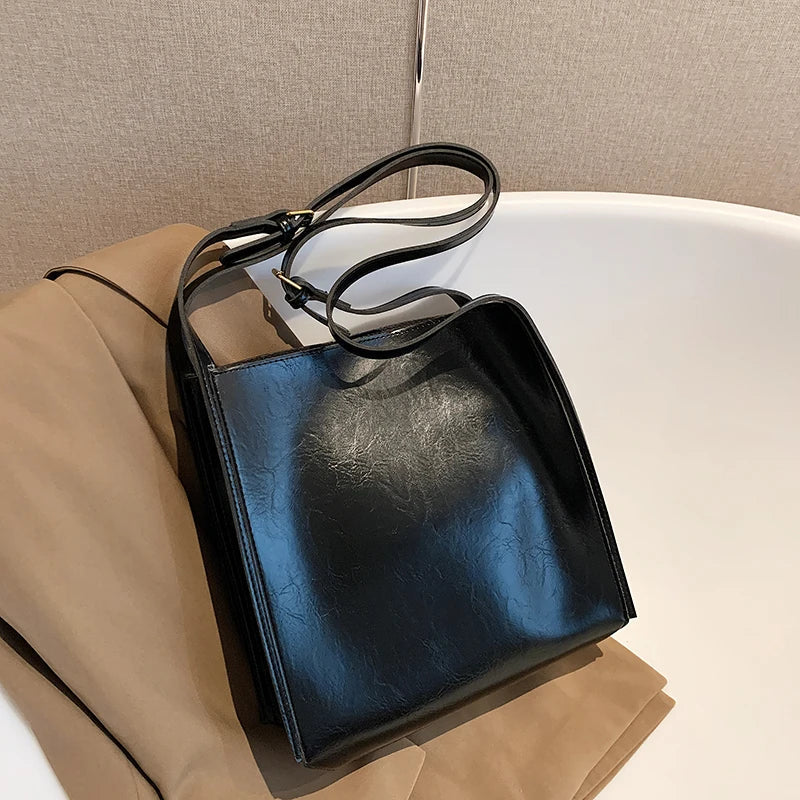 "Elegant damaxelväska i glänsande konstläder, modern design, justerbar rem, perfekt för både vardag och festliga tillfällen."