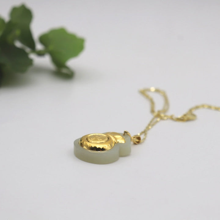 "Hängsmycke för kvinnor med Feng Shui inspiration, grön Hetian-jade och pengaväska symbol, i guldfärgad metall."