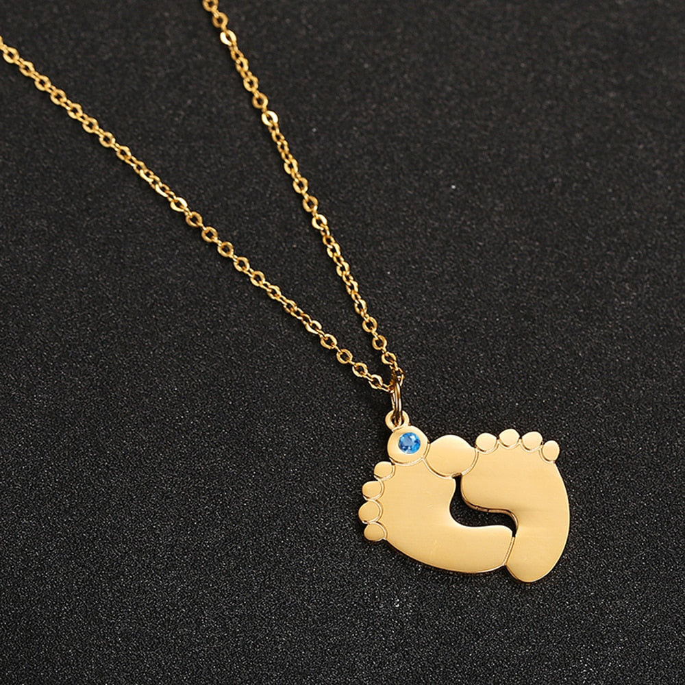 "Personligt halsband i guld med babyfötter och graverade namn, perfekt för mödrar, moderna och elegant design."