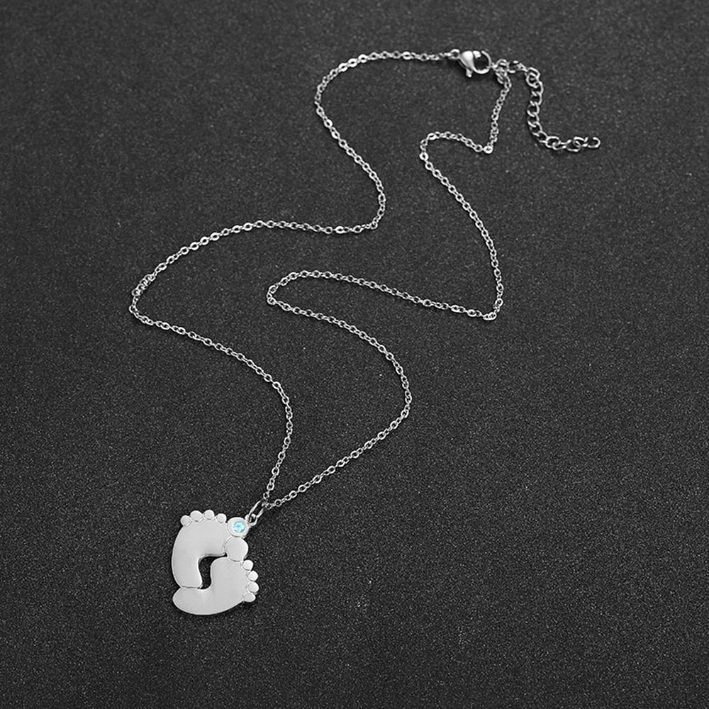 "Personligt halsband i guld med babyfötter och graverade namn, perfekt för mödrar, moderna och elegant design."
