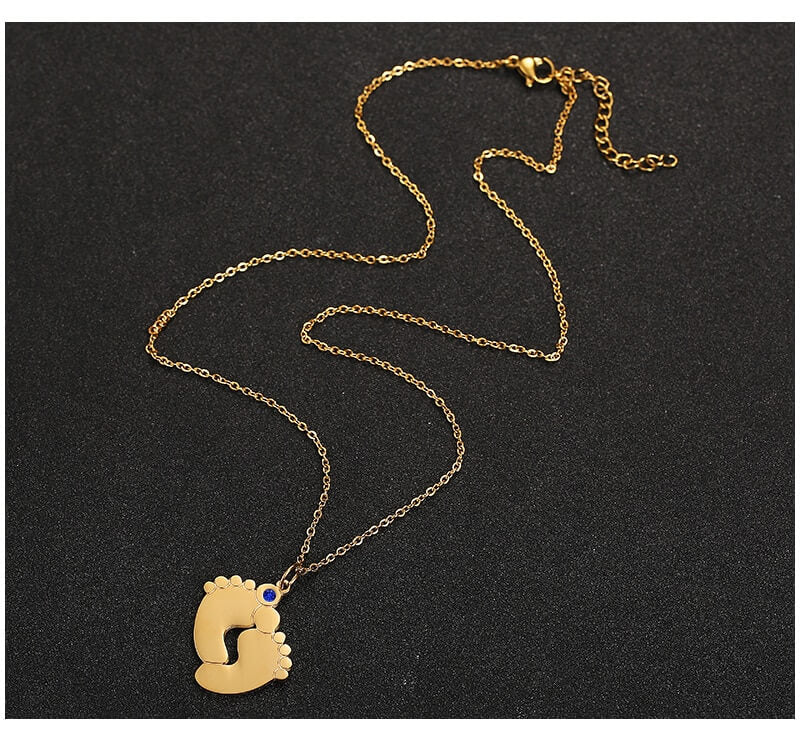 "Personligt halsband i guld med babyfötter och graverade namn, perfekt för mödrar, moderna och elegant design."