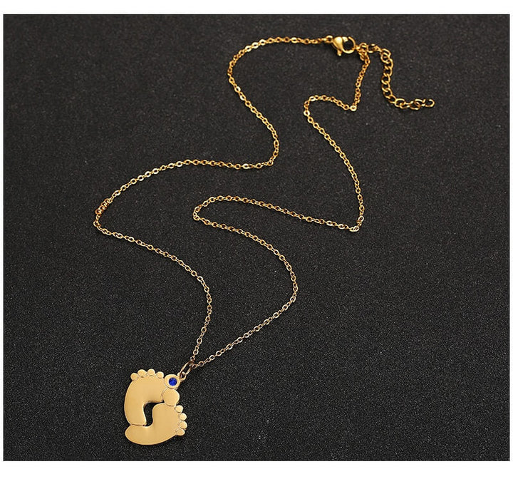 "Personligt halsband i guld med babyfötter och graverade namn, perfekt för mödrar, moderna och elegant design."