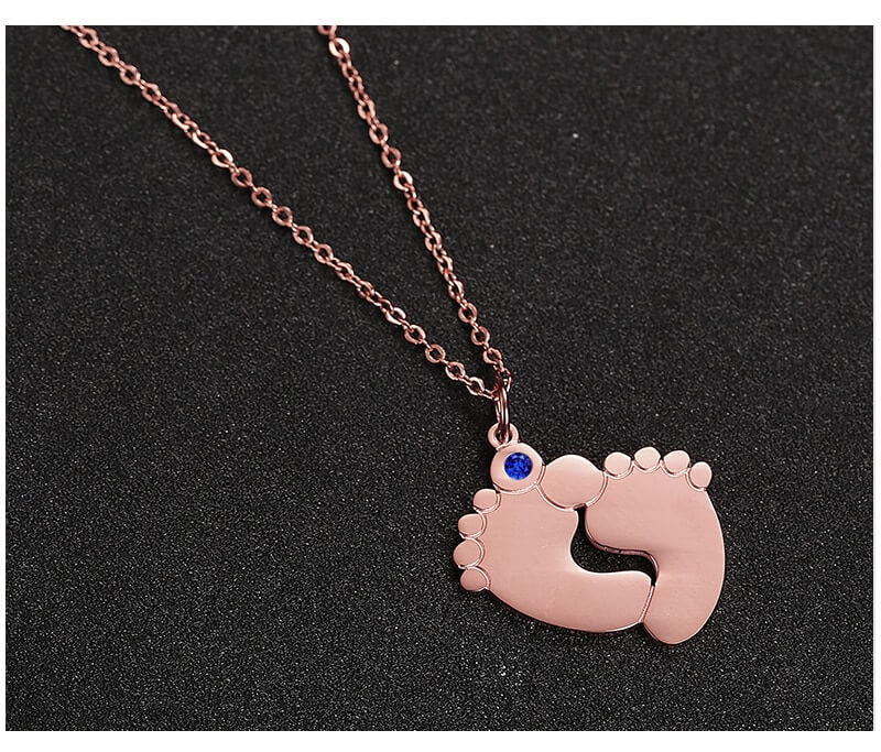 "Personligt halsband i guld med babyfötter och graverade namn, perfekt för mödrar, moderna och elegant design."
