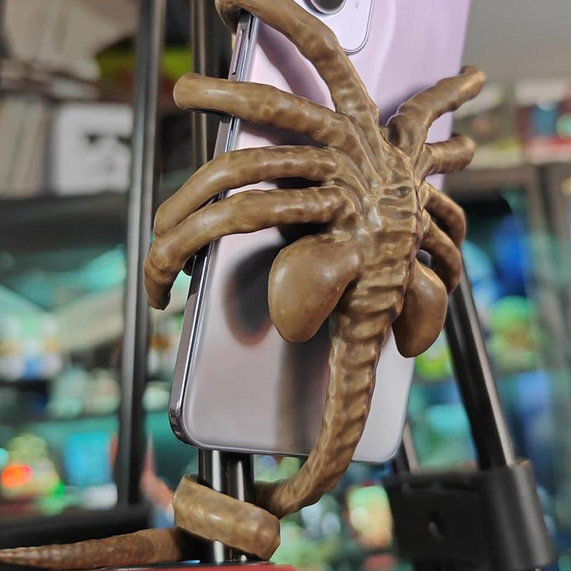 Alienformad telefonhållare i grön harts, passar alla smartphones; justerbar svans för stabilitet. Perfekt som present.