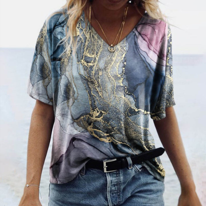 "Damtopp med sommarmarmortryck, V-ringning och utsvängd fåll, perfekt för stranddagar och vardagslook."