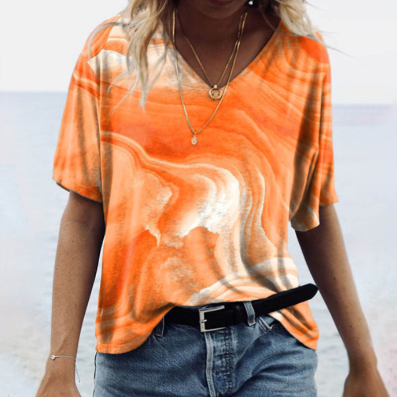 "Damtopp med sommarmarmortryck, V-ringning och utsvängd fåll, perfekt för stranddagar och vardagslook."