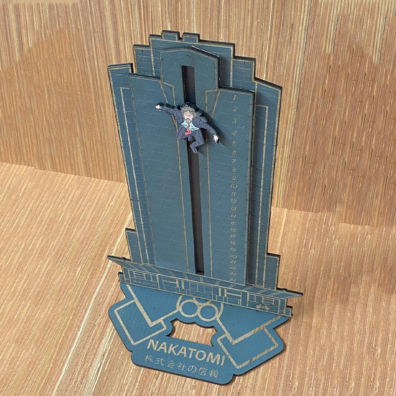 "Detaljerad trä Adventskalender med Die Hard-motiv, visar Hans Gruber faller från brunblå Nakatomi Plaza, roterbar design."