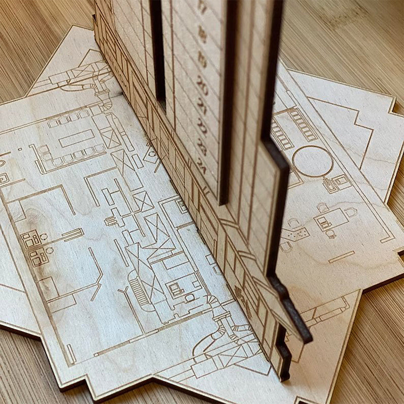 "Detaljerad trä Adventskalender med Die Hard-motiv, visar Hans Gruber faller från brunblå Nakatomi Plaza, roterbar design."