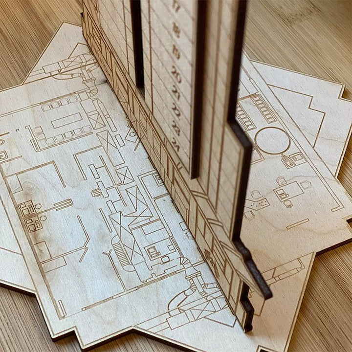 "Detaljerad trä Adventskalender med Die Hard-motiv, visar Hans Gruber faller från brunblå Nakatomi Plaza, roterbar design."