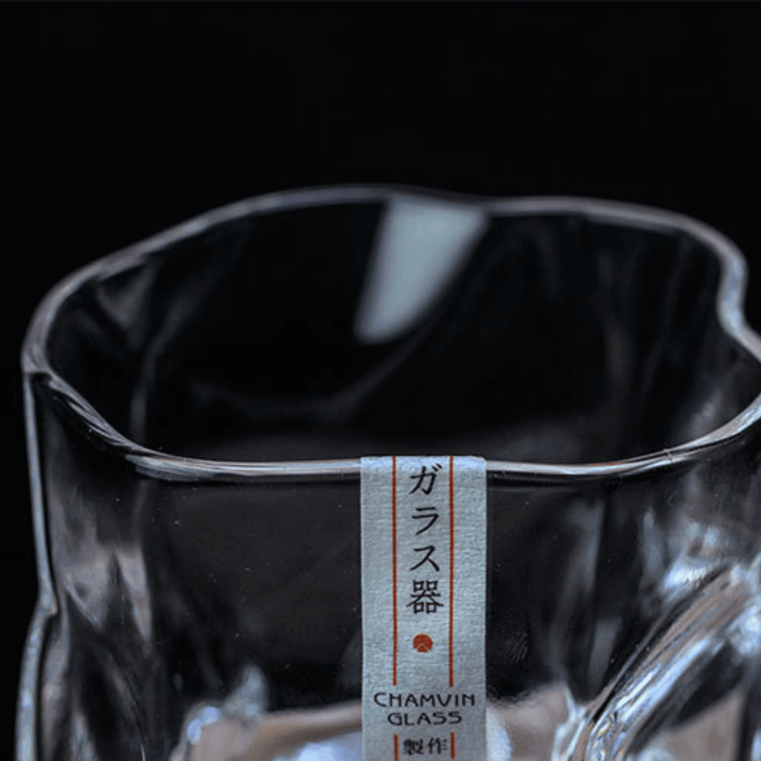 Unikt krökt Edo Kiriko whiskyglas i klarglas, reflekterar ljus vackert. Japanskt samlarobjekt.