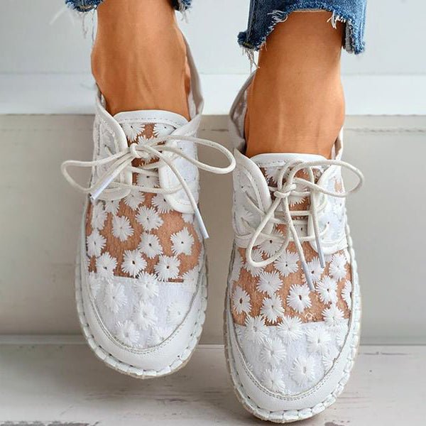 Närbild av vit kvinnorsneaker som visar detaljerade blom-broderier och snörning, perfekt för vår/höst