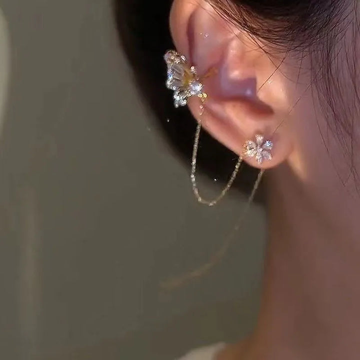 Guldpläterad öroncuff med detaljerad fjäril & blomma. Glittrande strass. Exklusiv damaccessoar utan piercing.