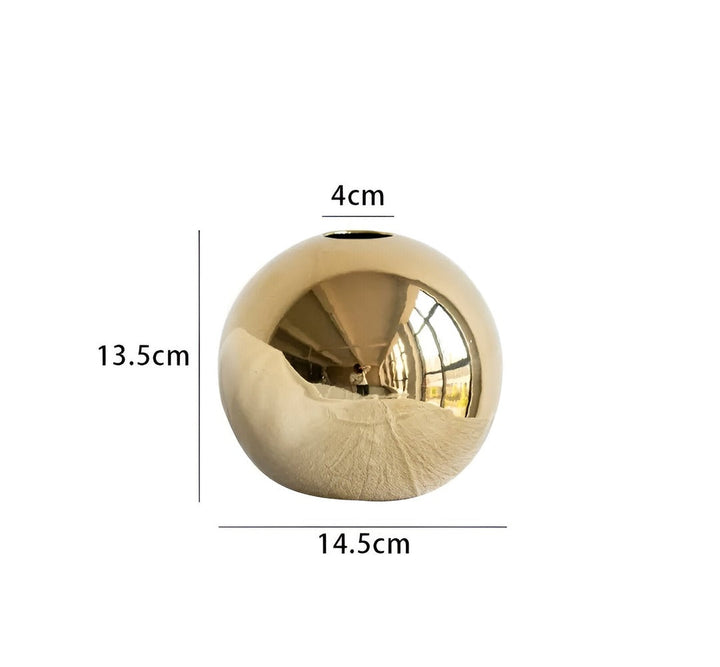 Minimalistisk rund gyllene vas i keramik, passar perfekt i ett modernt inrett vardagsrum som stilren dekoration.