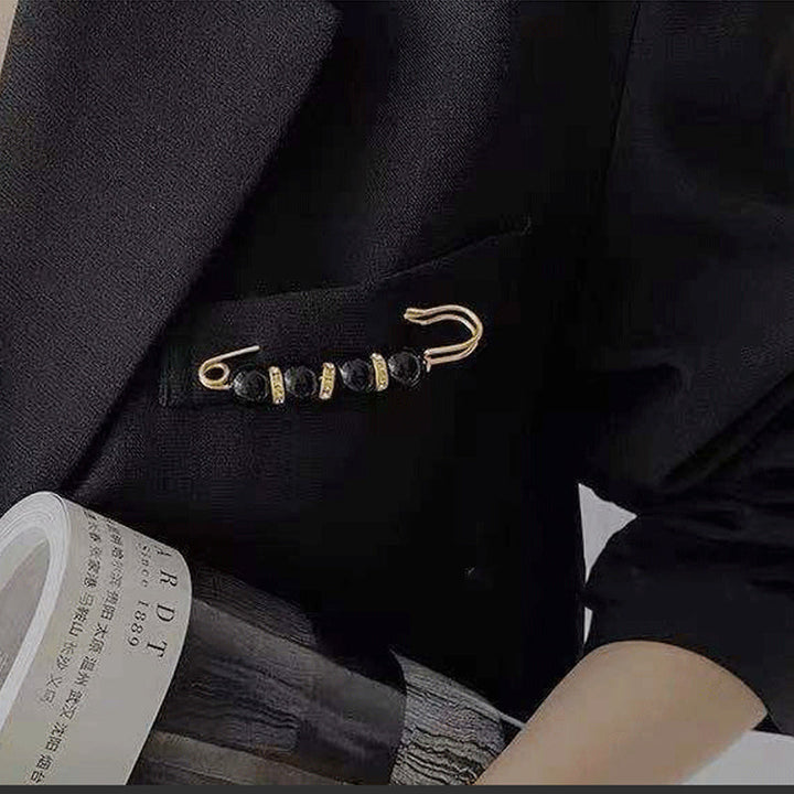 "Elegant säkerhetsnålsbrosch med vita pärlor och strass, perfekt för damkläder, i svart och vitt för stil och matchning."
