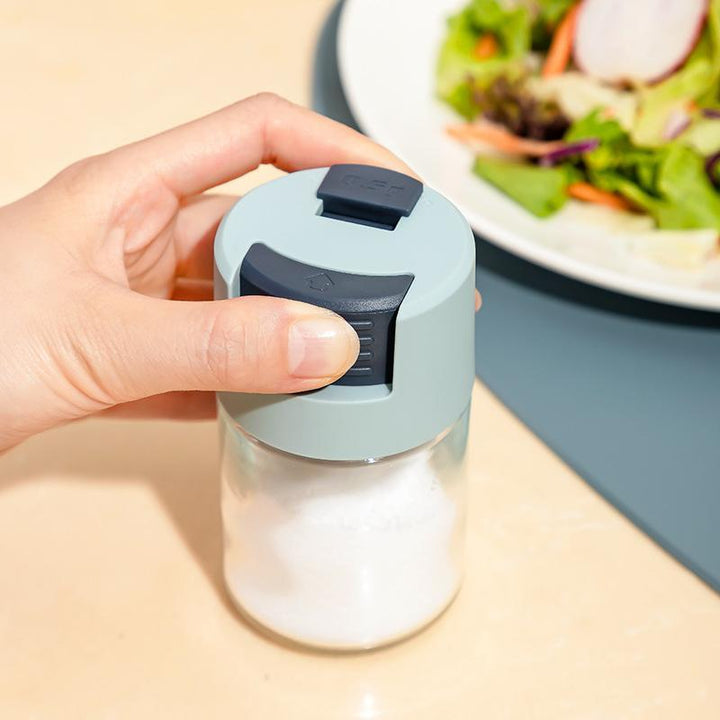 "Elegant saltkar i glas med mätfunktion, böjd form och modernt lock, perfekt för kryddförvaring i köket."