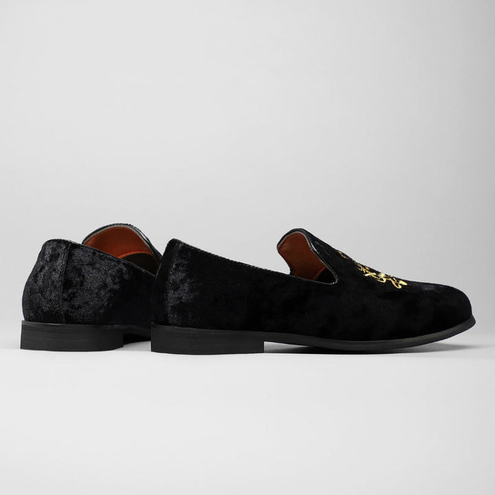 Nära bild av gyllene detalj på en slip-on loafer i svart sammet för herr, visar det exklusiva hantverket.