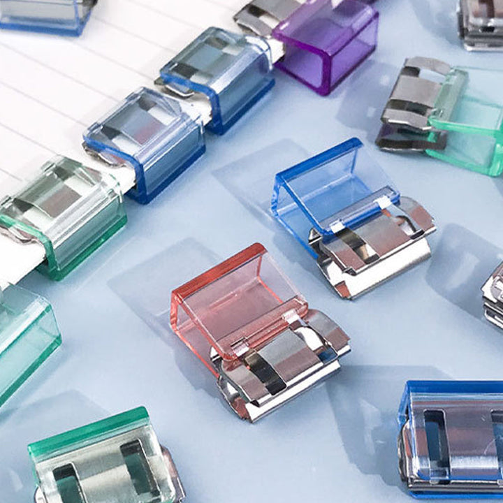 "Färgglada metallpappersklämmor i grönt, gult, lila, rosa, transparent och blått, perfekt för kontor och skola."