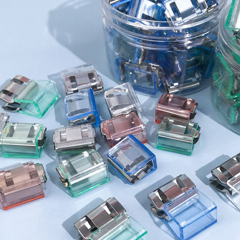 "Färgglada metallpappersklämmor i grönt, gult, lila, rosa, transparent och blått, perfekt för kontor och skola."