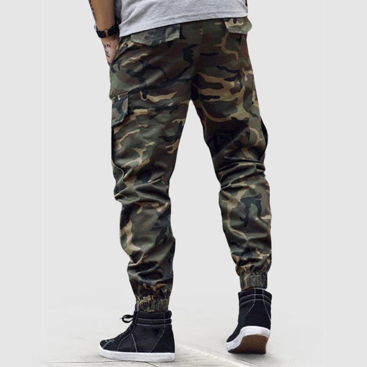 Man bär svarta kamouflage cargo joggers, poserar avslappnat, visar byxornas casual stil och komfort.