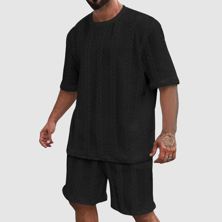 Man bär svart urban träningsdräkt med shorts och t-shirt, redo för fritidsaktiviteter.