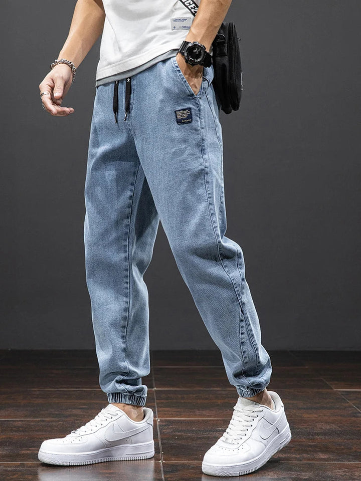 Stapel med olika färger av avslappnade herrjeans i denim. Svarta och blå alternativ för herrmode.