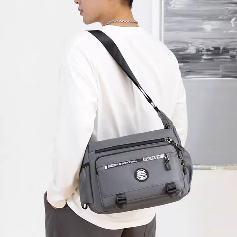 "Högkvalitativ svart axelväska för män med flera fickor, justerbara remmar och vattentät yta, sedd bakifrån."