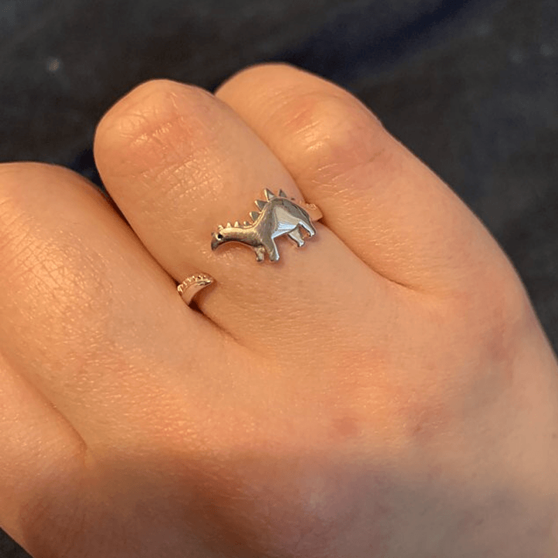"Justerbar dinosauriering i silver med dinosauriemotiv; elegant, lekfull och perfekt för dinosaurieälskare."