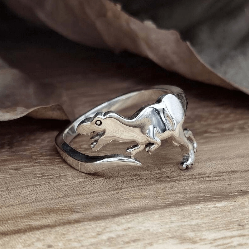 "Justerbar dinosauriering i silver med dinosauriemotiv; elegant, lekfull och perfekt för dinosaurieälskare."