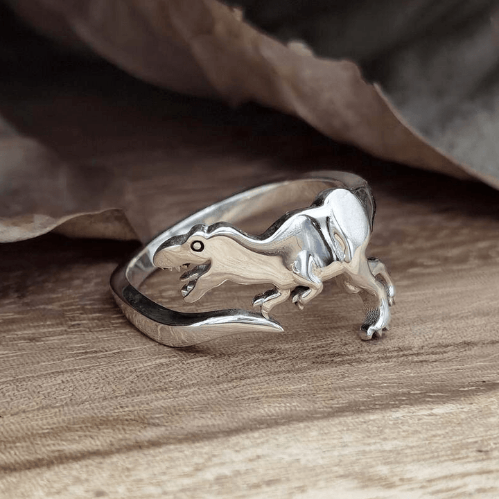 "Justerbar dinosauriering i silver med dinosauriemotiv; elegant, lekfull och perfekt för dinosaurieälskare."