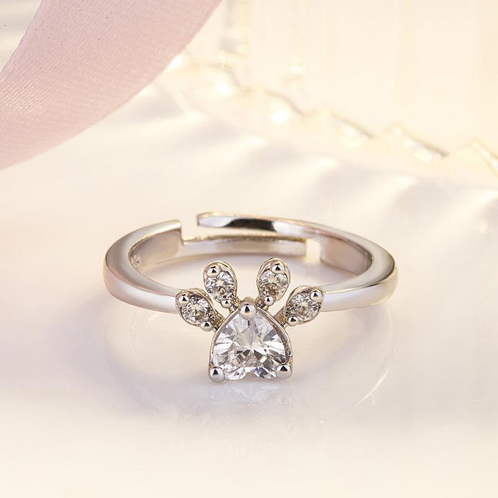 "Justerbar kattfotavtrycksring med zirkon, roséguld och vitt, elegant smycke för kattälskare."