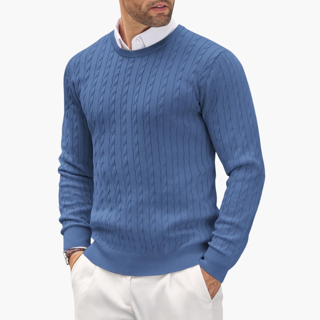 Man bär en stilren kabelstickad herrtröja med rund hals. Perfekt för en avslappnad men välklädd look.