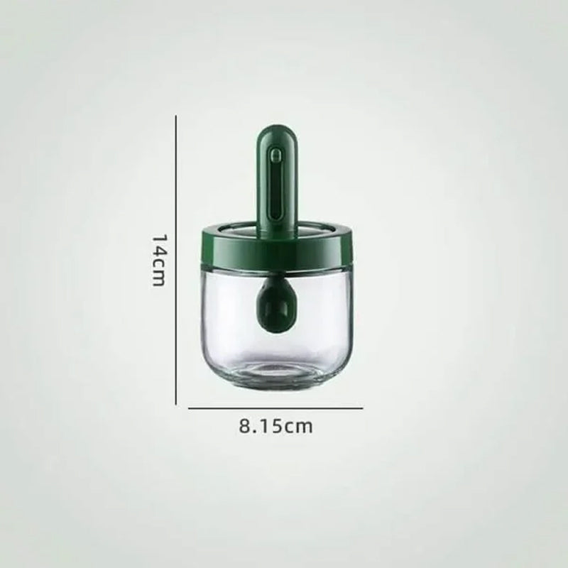 Kryddburk i glas med grönt och vitt skedlock, justerbart för enkel dosering, elegant design för köksanvändning.