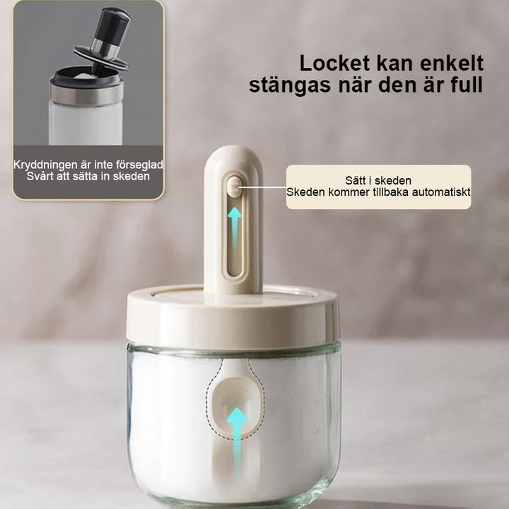 Kryddburk i glas med grönt och vitt skedlock, justerbart för enkel dosering, elegant design för köksanvändning.