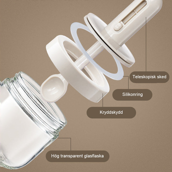 Kryddburk i glas med grönt och vitt skedlock, justerbart för enkel dosering, elegant design för köksanvändning.