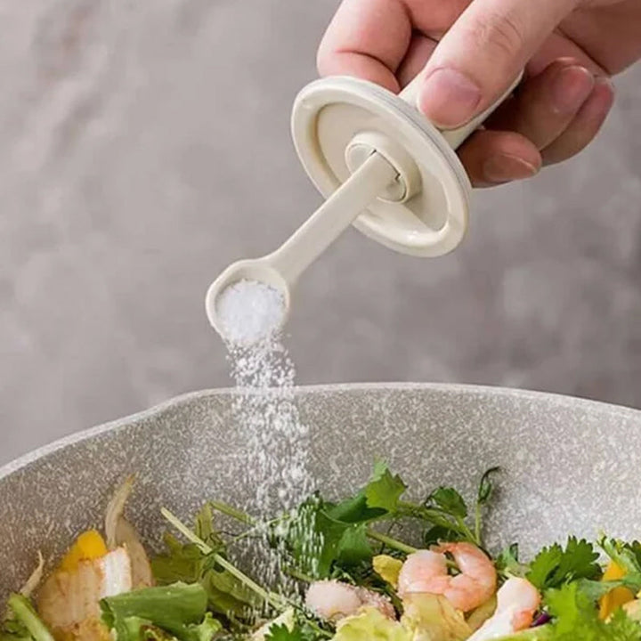 Kryddburk i glas med grönt och vitt skedlock, justerbart för enkel dosering, elegant design för köksanvändning.