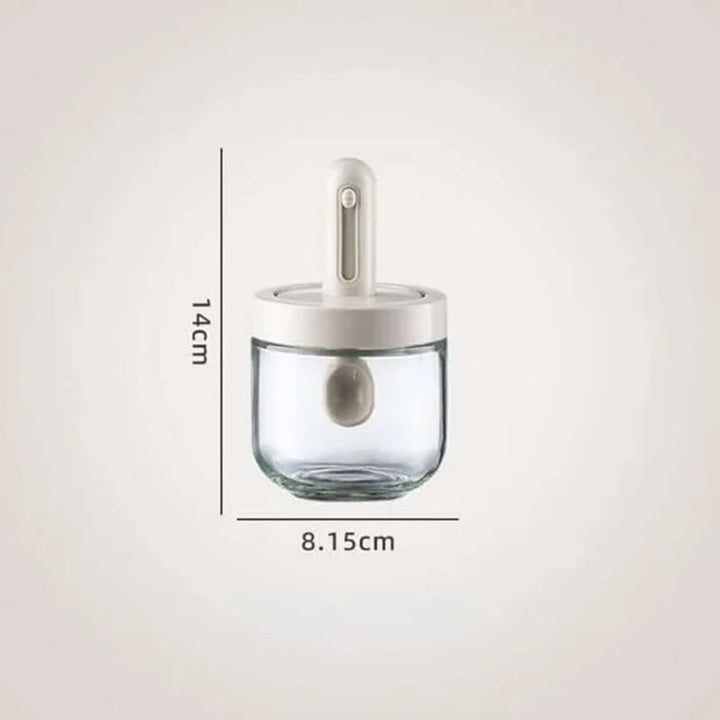 Kryddburk i glas med grönt och vitt skedlock, justerbart för enkel dosering, elegant design för köksanvändning.