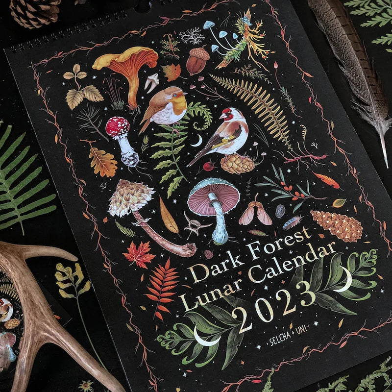 "Månkalender 2023 med mörka skogsmotiv, intrikata illustrationer, fångar natur och magi, fullmåne och stjärntecken."