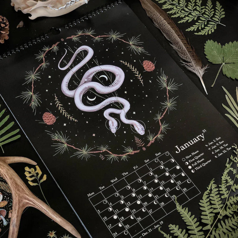 "Månkalender 2023 med mörka skogsmotiv, intrikata illustrationer, fångar natur och magi, fullmåne och stjärntecken."