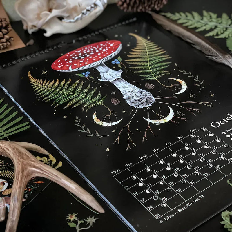 "Månkalender 2023 med mörka skogsmotiv, intrikata illustrationer, fångar natur och magi, fullmåne och stjärntecken."