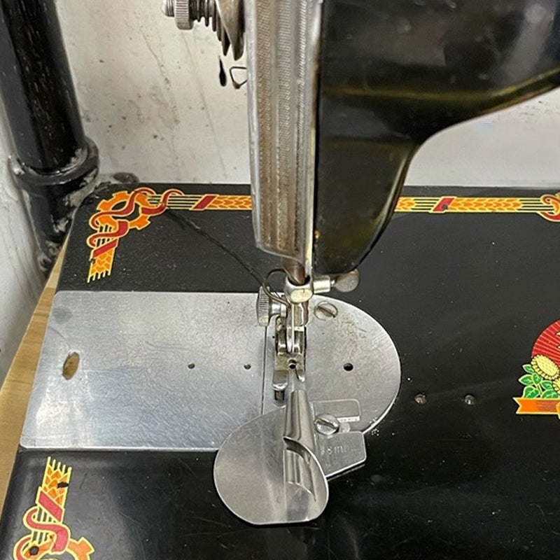 "Metallisk rullad sömspressarfot för sömnad, visad med tyg, för exakta fållar. Perfekt för både tunna och tjockare tyger."