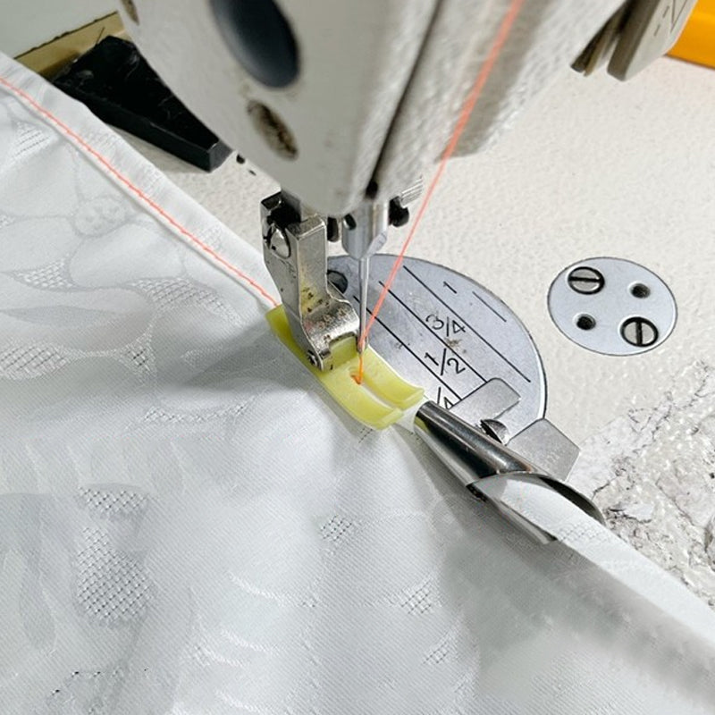 "Metallisk rullad sömspressarfot för sömnad, visad med tyg, för exakta fållar. Perfekt för både tunna och tjockare tyger."