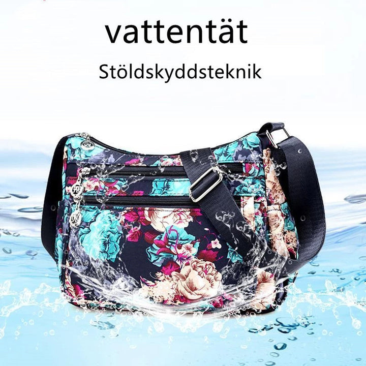 "Mönstrad damväska i vattentätt nylon med justerbar axelrem och flera fack, svart blommigt mönster."