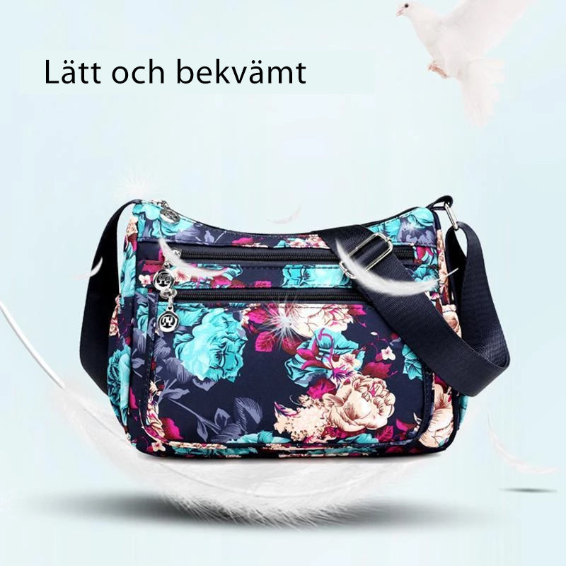 "Mönstrad damväska i vattentätt nylon med justerbar axelrem och flera fack, svart blommigt mönster."