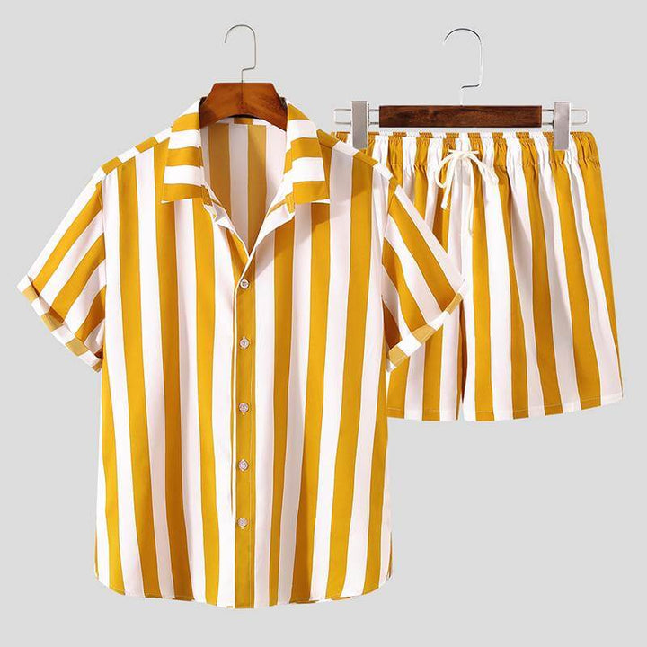 Man i randigt sommarset (kortärmad skjorta & shorts) kopplar av på stranden, perfekt semesteroutfit.