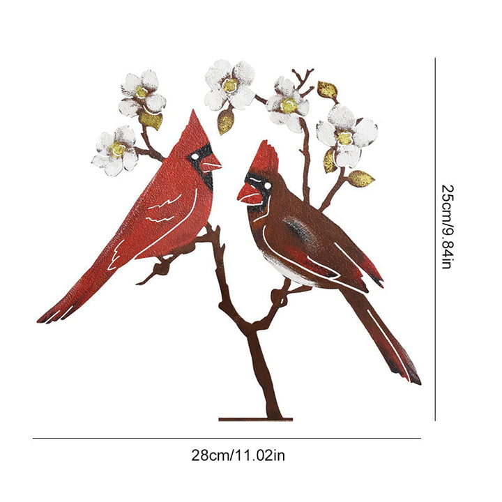 "Röd fågelprydnad i järn, handmålad, visar livfull design i trädgården bland färgglada blommor."