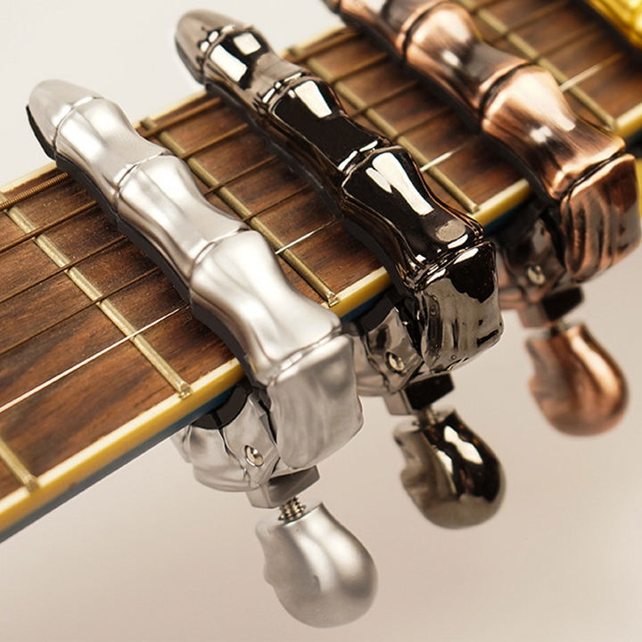 Skalleformad gitarrcapo i metall med unik design, perfekt för akustiska och elektriska gitarrer, finns i flera färger.