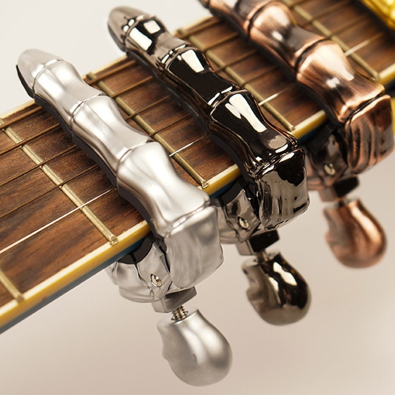 Skalleformad gitarrcapo i metall med unik design, perfekt för akustiska och elektriska gitarrer, finns i flera färger.