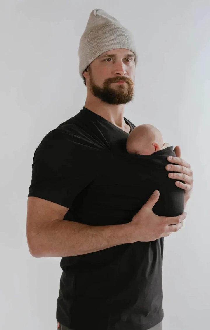 Mamma bär sin baby i CarrySeed Tee bärsele, visar ergonomisk design för säker och snugfit komfort.