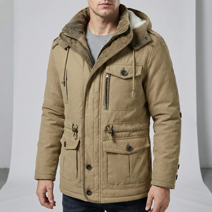 Man bär en stilren beige herrparka "Dylan" med huva och muddar. Vinterjacka för kalla dagar.